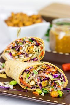 there are two wraps on the plate with carrots and other foods in the background