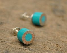 two turquoise and gold ear studs laying on top of a sandy beach covered in sand