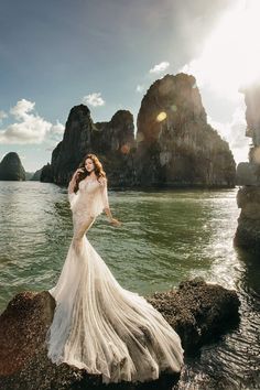 a woman standing on top of a rock next to the ocean wearing a white dress