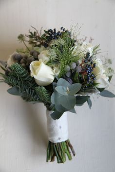 a bridal bouquet with white roses, greenery and blue berries sits on the wall