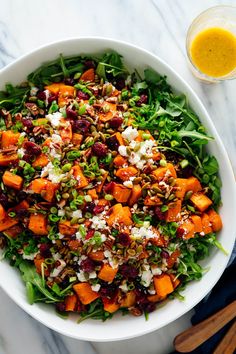 a white bowl filled with greens and sweet potato salad next to a glass of orange juice