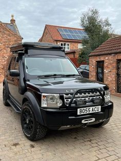 a black land rover parked in front of a brick building with solar panels on the roof