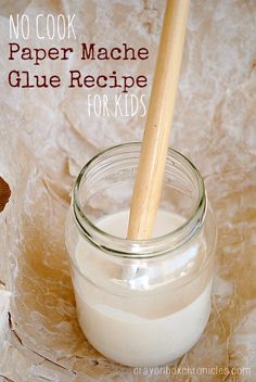 a glass jar filled with white liquid next to a wooden spoon on top of a table