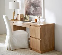 a white chair sitting next to a desk with a painting on it's wall