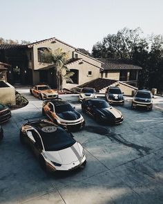 a group of exotic cars parked in front of a house with palm trees on the driveway