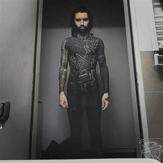 a man with tattoos standing in an open door to another room, looking at the camera