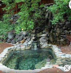 a small pond in the middle of a garden with rocks and water flowing from it