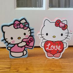 two hello kitty magnets sitting next to each other on a wooden floor in front of a door