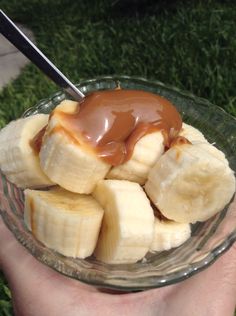 a person holding a glass bowl filled with sliced bananas and caramel sauce on top