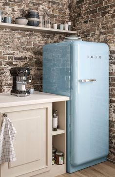 a blue refrigerator in a kitchen next to a brick wall and white counter top with dishes on it