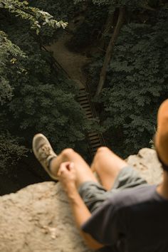 a man sitting on top of a rock next to a forest filled with green trees