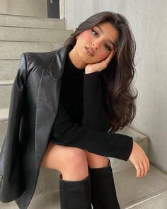 a woman sitting on the steps with her legs crossed and wearing black over the knee boots