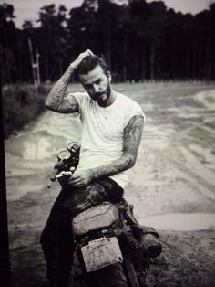 a black and white photo of a man sitting on a motorbike in the mud