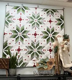 a christmas quilt hanging on the wall next to a chair and potted plant in front of it