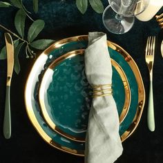 a place setting with green and gold plates, silverware and napkins on a black table cloth