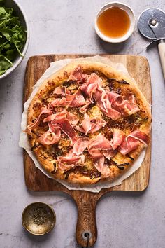 a pizza sitting on top of a wooden cutting board next to bowls of salad and utensils