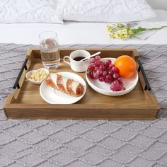 a tray with grapes, oranges and bread on it next to a glass of water