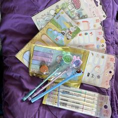 some pens and other items are laying on a purple bed sheet with hello kitty stickers