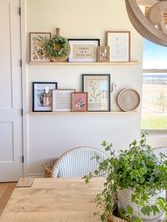 a dining room table and chairs with pictures on the wall above it, next to a potted plant