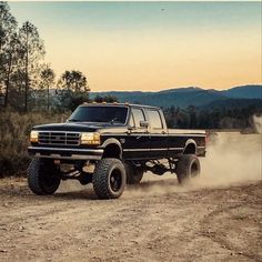 a black truck driving down a dirt road