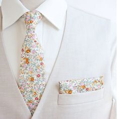 a man wearing a white suit with a floral tie and pocket square on his lapel