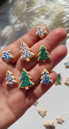 small decorated cookies in the shape of christmas trees on a person's hand with white and blue sprinkles