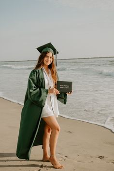 a woman in a graduation cap and gown standing on the beach with her diploma certificate