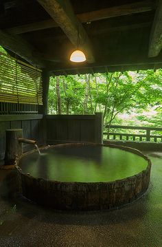 an outdoor hot tub in the middle of a covered area with trees and bushes behind it