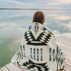 a woman wrapped in a blanket sitting on a dock