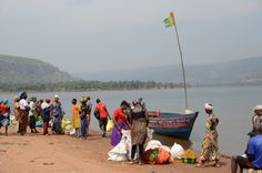 a group of people standing next to a body of water with a boat in the background