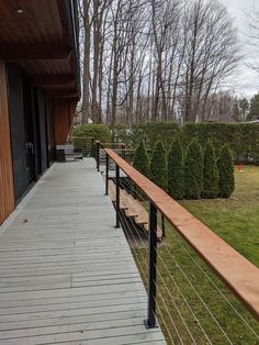 a wooden deck with metal railings next to a green lawn and trees in the background