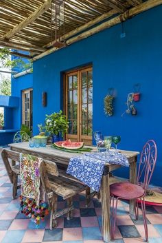 an outdoor dining area with blue walls and tile flooring, including a wooden table surrounded by colorful chairs