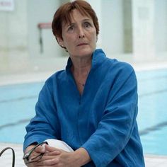 a woman sitting on the edge of a swimming pool holding a frisbee in her hand