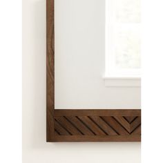 a wooden mirror hanging on the wall next to a white wall with a window in it