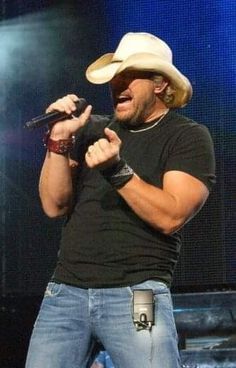 a man wearing a cowboy hat and holding a microphone in his right hand while standing on stage