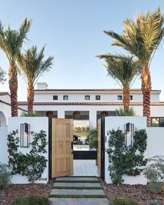 an open door leading to a white house with palm trees in the front yard and walkway