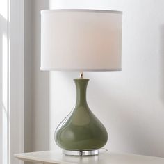 a green lamp sitting on top of a table next to a white wall and window