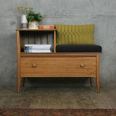 a wooden bench sitting next to a wall with books on it and a green cushion