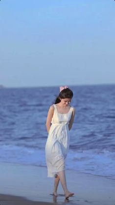 a woman is walking on the beach talking on her cell phone while wearing a white dress