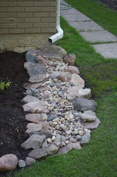 a rock garden bed in front of a house with green grass and rocks around it