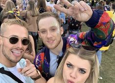 two men and a woman posing for the camera at an outdoor music festival with their hands in the air