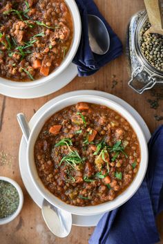 two white bowls filled with soup on top of a wooden table next to spoons