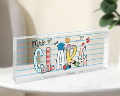 a glass name plate with the word class written in colorful letters and graduation caps on it