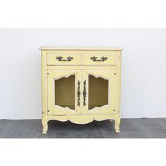 an old yellow cabinet with glass doors and drawers on the bottom, in front of a white wall