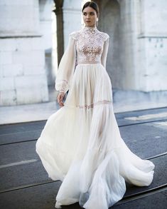 a woman in a long white dress is standing on the street with her hands behind her back