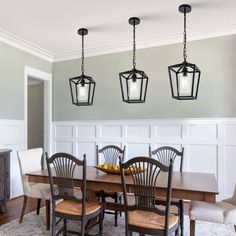 a dining room table and chairs with four hanging lights