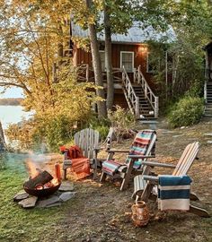 there are many lawn chairs and fire pit in front of the cabin on the lake