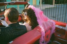 a man and woman sitting in the back of a red convertible car with pink feathers