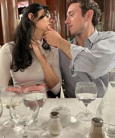 a man and woman sitting at a table with wine glasses in front of their faces