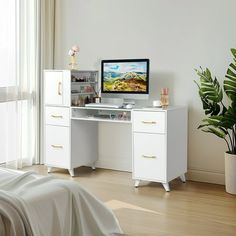 a white desk with a computer monitor and keyboard on it next to a potted plant